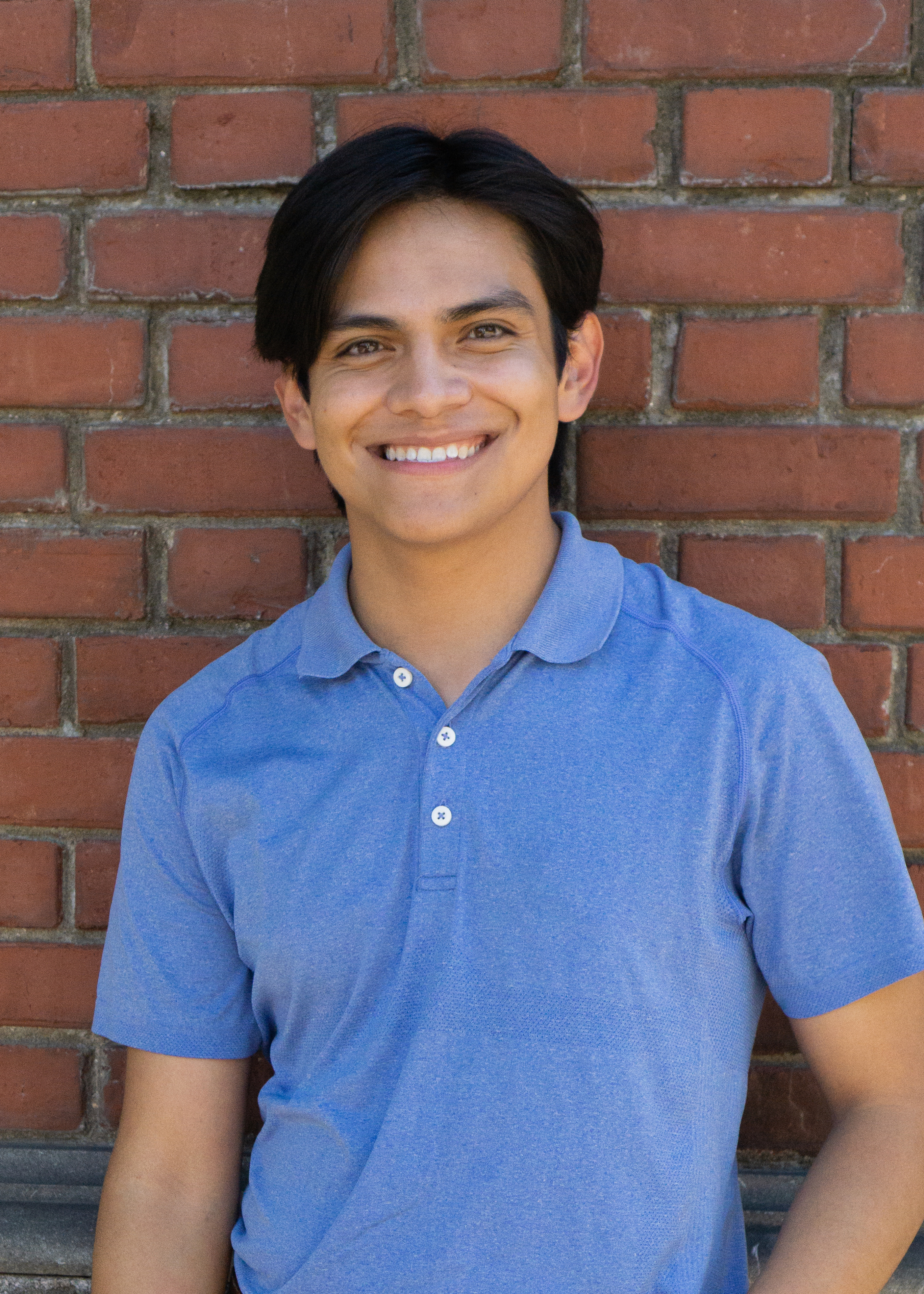 Carlos poses in front of a brick wall.